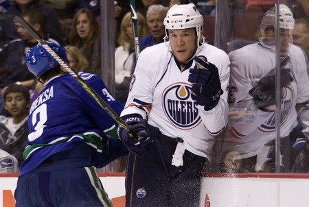 VANCOUVER, CANADA - SEPTEMBER 19:  Steve MacIntyre #33 of the Edmonton Oilers reacts after getting hit into the end boards by Kevin Bieksa #3 of the Vancouver Canucks during the first period of NHL preseason action on September 19, 2009 at General Motors Place in Vancouver, British Columbia, Canada.  <br /><br /><span class="help">(Photo by Rich Lam/Getty Images)</span>
