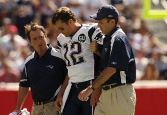 FOXBORO, MA - SEPTEMBER 7:  Quarterback Tom Brady #12 of the New England Patriots is helped off the field by trainers after he sustained an injury to his left knee in the first quarter against the Kansas City Chiefs at Gillette Stadium September 7, 2008 in Foxboro, Massachusetts.  (Photo by Elsa/Getty Images)