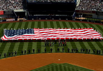 NEW YORK - APRIL 16:  Recording artist Kelly Clarkson sings the National Anthem as members of the military hold a giant American flag before the opening day game between the Cleveland Indians and the New York Yankees at the new Yankee Stadium on April 16, 2009 in the Bronx borough of New York City. This is the first regular season MLB game being played at the new venue which replaced the old Yankee Stadium as the Yankees home field.  (Photo by Nick Laham/Getty Images)