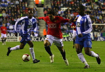 WIGAN, ENGLAND - MAY 13:  Carlos Tevez of Manchester United beats Titus Bramble and Maynor Figueroa of Wigan Athletic during the Barclays Premier League match between Wigan Athletic and Manchester United at the JJB Stadium on May 13, 2009 in Wigan, England.  (Photo by Alex Livesey/Getty Images)