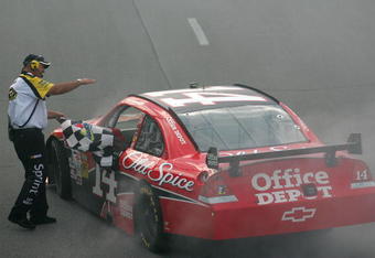 LONG POND, PA - JUNE 07:  Tony Stewart, driver of the #14 Office Depot/Old Spice Chevrolet, takes the checkered flag from a NASCAR official after winning the NASCAR Sprint Cup Series Pocono 500 on June 7, 2009 at Pocono Raceway in Long Pond, Pennsylvania.  (Photo by Todd Warshaw/Getty Images)
