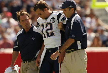 FOXBORO, MA - SEPTEMBER 7:  Quarterback Tom Brady #12 of the New England Patriots is helped off the field by trainers after he sustained an injury to his left knee in the first quarter against the Kansas City Chiefs at Gillette Stadium September 7, 2008 in Foxboro, Massachusetts.  (Photo by Elsa/Getty Images)