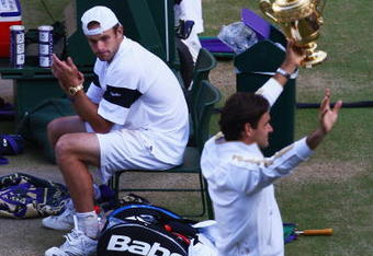 WIMBLEDON, ENGLAND - JULY 05:  Andy Roddick of USA looks despondent as Roger Federer of Switzerland celebrates with the trophy during the men's singles final match on Day Thirteen of the Wimbledon Lawn Tennis Championships at the All England Lawn Tennis and Croquet Club on July 5, 2009 in London, England. Federer won 5-7, 7-6, 7-6, 3-6, 16-14.  (Photo by Julian Finney/Getty Images)