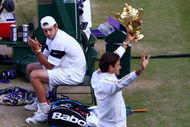WIMBLEDON, ENGLAND - JULY 05:  Andy Roddick of USA looks despondent as Roger Federer of Switzerland celebrates with the trophy during the men's singles final match on Day Thirteen of the Wimbledon Lawn Tennis Championships at the All England Lawn Tennis and Croquet Club on July 5, 2009 in London, England. Federer won 5-7, 7-6, 7-6, 3-6, 16-14.  (Photo by Julian Finney/Getty Images)