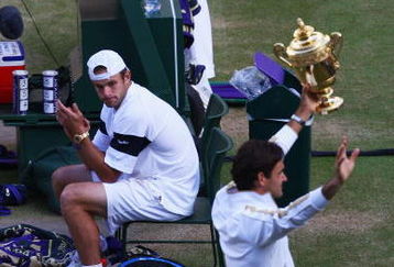 WIMBLEDON, ENGLAND - JULY 05:  Andy Roddick of USA looks despondent as Roger Federer of Switzerland celebrates with the trophy during the men's singles final match on Day Thirteen of the Wimbledon Lawn Tennis Championships at the All England Lawn Tennis and Croquet Club on July 5, 2009 in London, England. Federer won 5-7, 7-6, 7-6, 3-6, 16-14.  (Photo by Julian Finney/Getty Images)