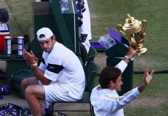 WIMBLEDON, ENGLAND - JULY 05:  Andy Roddick of USA looks despondent as Roger Federer of Switzerland celebrates with the trophy during the men's singles final match on Day Thirteen of the Wimbledon Lawn Tennis Championships at the All England Lawn Tennis and Croquet Club on July 5, 2009 in London, England. Federer won 5-7, 7-6, 7-6, 3-6, 16-14.  (Photo by Julian Finney/Getty Images)