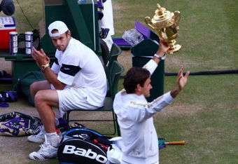 WIMBLEDON, ENGLAND - JULY 05:  Andy Roddick of USA looks despondent as Roger Federer of Switzerland celebrates with the trophy during the men's singles final match on Day Thirteen of the Wimbledon Lawn Tennis Championships at the All England Lawn Tennis and Croquet Club on July 5, 2009 in London, England. Federer won 5-7, 7-6, 7-6, 3-6, 16-14.  (Photo by Julian Finney/Getty Images)