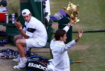 WIMBLEDON, ENGLAND - JULY 05:  Andy Roddick of USA looks despondent as Roger Federer of Switzerland celebrates with the trophy during the men's singles final match on Day Thirteen of the Wimbledon Lawn Tennis Championships at the All England Lawn Tennis and Croquet Club on July 5, 2009 in London, England. Federer won 5-7, 7-6, 7-6, 3-6, 16-14.  (Photo by Julian Finney/Getty Images)