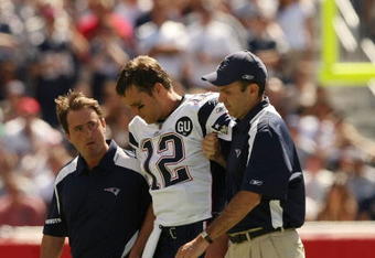 FOXBORO, MA - SEPTEMBER 7:  Quarterback Tom Brady #12 of the New England Patriots is helped off the field by trainers after he sustained an injury to his left knee in the first quarter against the Kansas City Chiefs at Gillette Stadium September 7, 2008 in Foxboro, Massachusetts.  (Photo by Elsa/Getty Images)