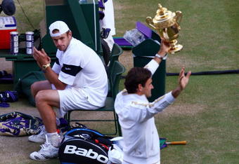 WIMBLEDON, ENGLAND - JULY 05:  Andy Roddick of USA looks despondent as Roger Federer of Switzerland celebrates with the trophy during the men's singles final match on Day Thirteen of the Wimbledon Lawn Tennis Championships at the All England Lawn Tennis and Croquet Club on July 5, 2009 in London, England. Federer won 5-7, 7-6, 7-6, 3-6, 16-14.  (Photo by Julian Finney/Getty Images)