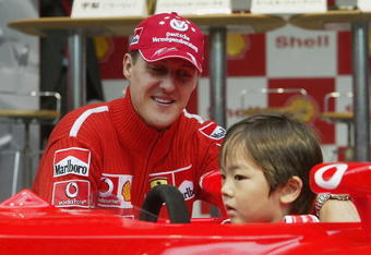 TOKYO - OCTOBER 8:  Michael Schumacher of Germany and Ferrari poses on Stage with a local child during an appearance at the Showa Shell headquarters on October 8, 2003 in Tokyo, Japan. (Photo by Mark Thompson/Getty Images).