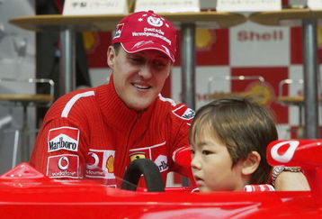 TOKYO - OCTOBER 8:  Michael Schumacher of Germany and Ferrari poses on Stage with a local child during an appearance at the Showa Shell headquarters on October 8, 2003 in Tokyo, Japan. (Photo by Mark Thompson/Getty Images).
