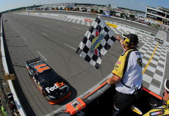 LONG POND, PA - AUGUST 03:  Denny Hamlin, driver of the #11 Federal Express Toyota, comes to the finish line to take the checkered flag from NASCAR flagman Rick Monroe as he took victory in the NASCAR Sprint Cup Series Sunoco Red Cross Pennsylvania 500 at the Pocono Raceway on August 3, 2009 in Long Pond, Pennsylvania.  (Photo by Doug Pensinger/Getty Images)
