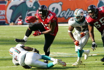 MIAMI - NOVEMBER 6:  Tight end Alge Crumpler #83 of the Atlanta Falcons jumps over cornerback Travis Daniels #21 of the Miami Dolphins after a pass reception on November 6, 2005 at Dolphins Stadium in Miami, Florida. The Falcons defeated the Dolphins 17-10. (Photo by Paul Spinelli/Getty Images)