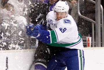LOS ANGELES, CA - OCTOBER 29:  Rob Scuderi #7 of the Los Angeles Kings is checked into the boards by Alexandre Bolduc #49 of the Vancouver Canucks in the first period at Staples Center on October 29, 2009 in Los Angeles, California.  (Photo by Jeff Gross/Getty Images)