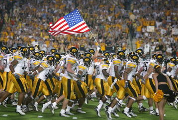 MIAMI - JANUARY 2:  The Iowa Hawkeyes take the field against USC as a team member holds the United States flag before the FedEx Orange Bowl on January 2, 2003 at Pro Player Stadium in Miami, Florida.  USC defeated Iowa 38-17.  (Photo by Eliot J. Schechter/Getty Images)
