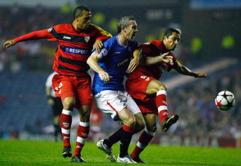 GLASGOW, SCOTLAND - SEPTEMBER 29:  David Weir of Rangers tackles Luis Fabiano and Adriano of Sevilla during the UEFA Champions League Group G match between Rangers and Sevilla at Ibrox Stadium on September 29, 2009 in Glasgow, Scotland.  (Photo by Jeff J Mitchell/Getty Images)