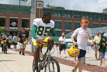 GREEN BAY, WI - AUGUST 03: Greg Jennings #85 of the Green Bay Packers rides a bike to practice as a young fan carries his helmut during summer training camp on August 3, 2009 at the Ray Nitschke Field in Green Bay, Wisconsin. (Photo by Jonathan Daniel/Getty Images)