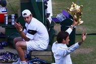 WIMBLEDON, ENGLAND - JULY 05:  Andy Roddick of USA looks despondent as Roger Federer of Switzerland celebrates with the trophy during the men's singles final match on Day Thirteen of the Wimbledon Lawn Tennis Championships at the All England Lawn Tennis and Croquet Club on July 5, 2009 in London, England. Federer won 5-7, 7-6, 7-6, 3-6, 16-14.  (Photo by Julian Finney/Getty Images)