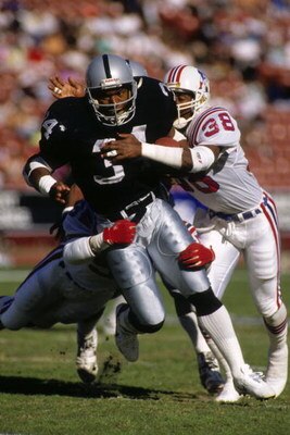 LOS ANGELES - NOVEMBER 26:  Bo Jackson #34 of the Los Angeles Raiders tries to break a tackle New by England Patriots defensive end Roland James #38 at the Los Angeles Memorial Coliseum on November 26, 1989 in Los Angeles, California. The Raiders won 24-2